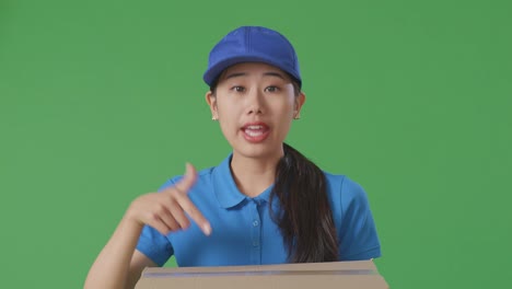 close up of unsatisfied asian female courier in blue uniform shouting to camera while delivering a carton on green screen background in the studio