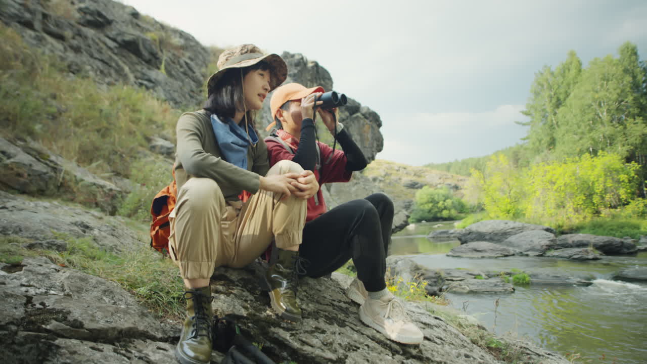 Female Hikers Using Binoculars on River Bank