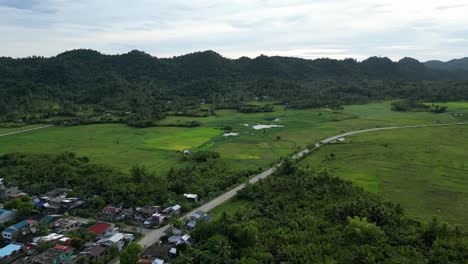 aerial establishing shot of rural island town connected to long winding road with lush rice paddies and mountains in background