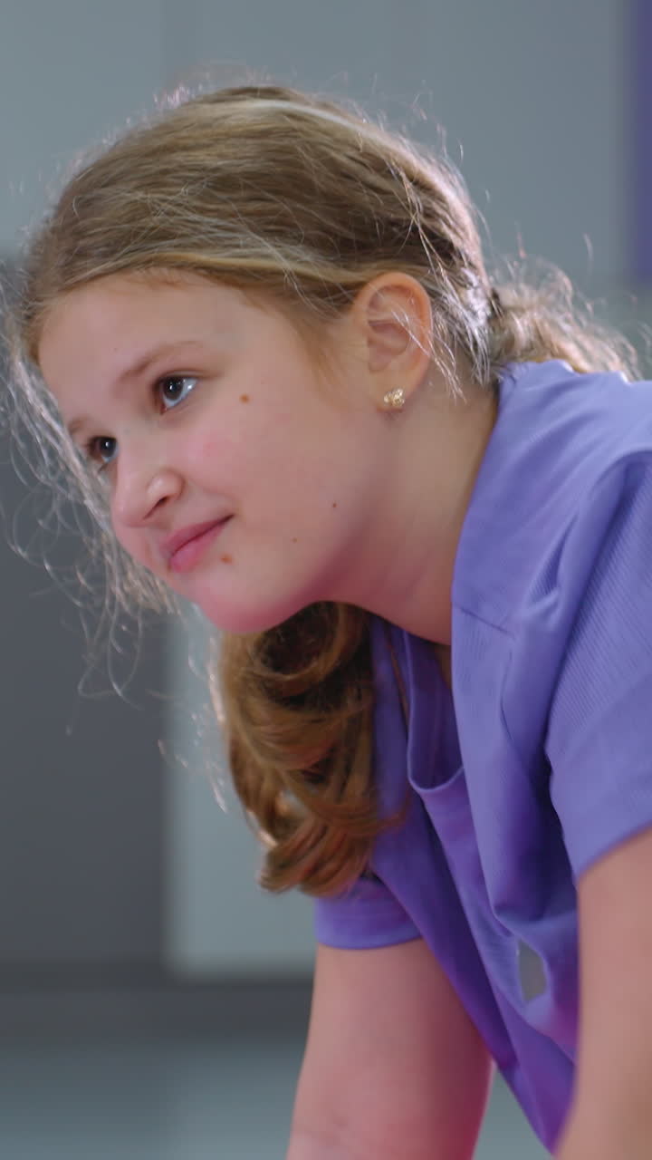 Primo piano ravvicinato di una bambina che estende la mano in avanti durante un esercizio di equilibrio con un blocco viola sulla schiena, enfatizzando la concentrazione e l'equilibrio.