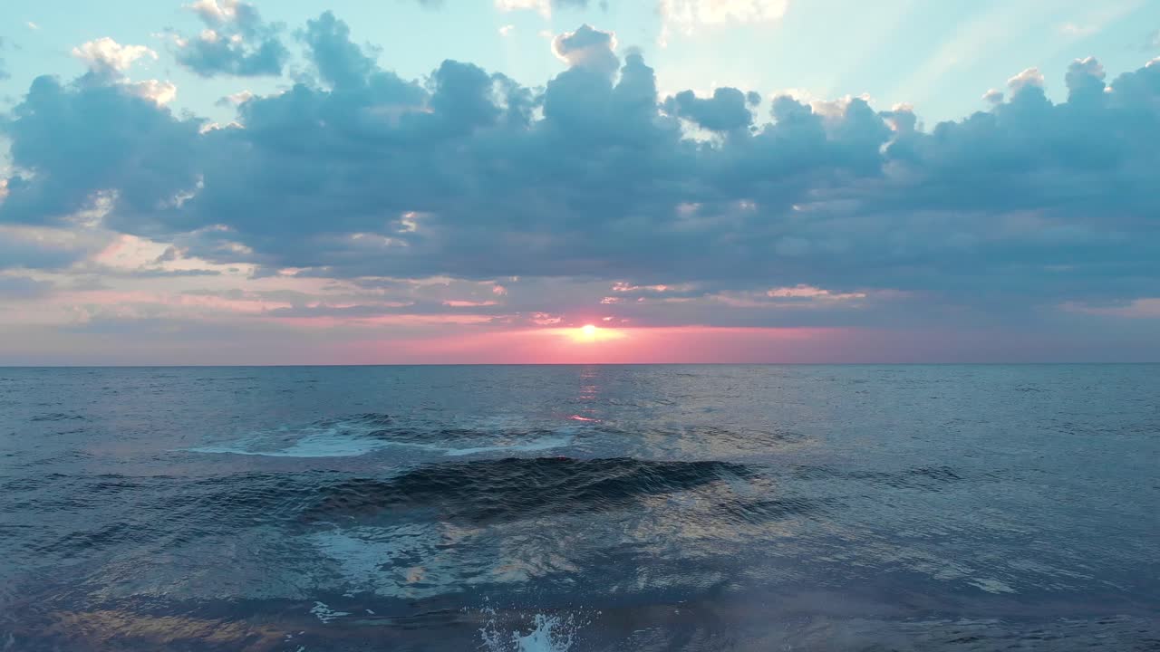 Aerial shot of a gorgeous sunrise, flying very close to the sea. Dolly out, tilt down