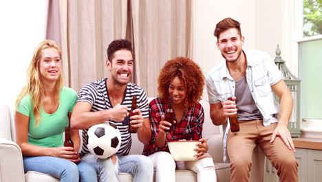 smiling friends watching tv while eating popcorn and drinking beer