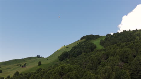 a lone paraglider soars high above a forested mountain slope with a clear blue sky in the background, epitomizing freedom and adventure