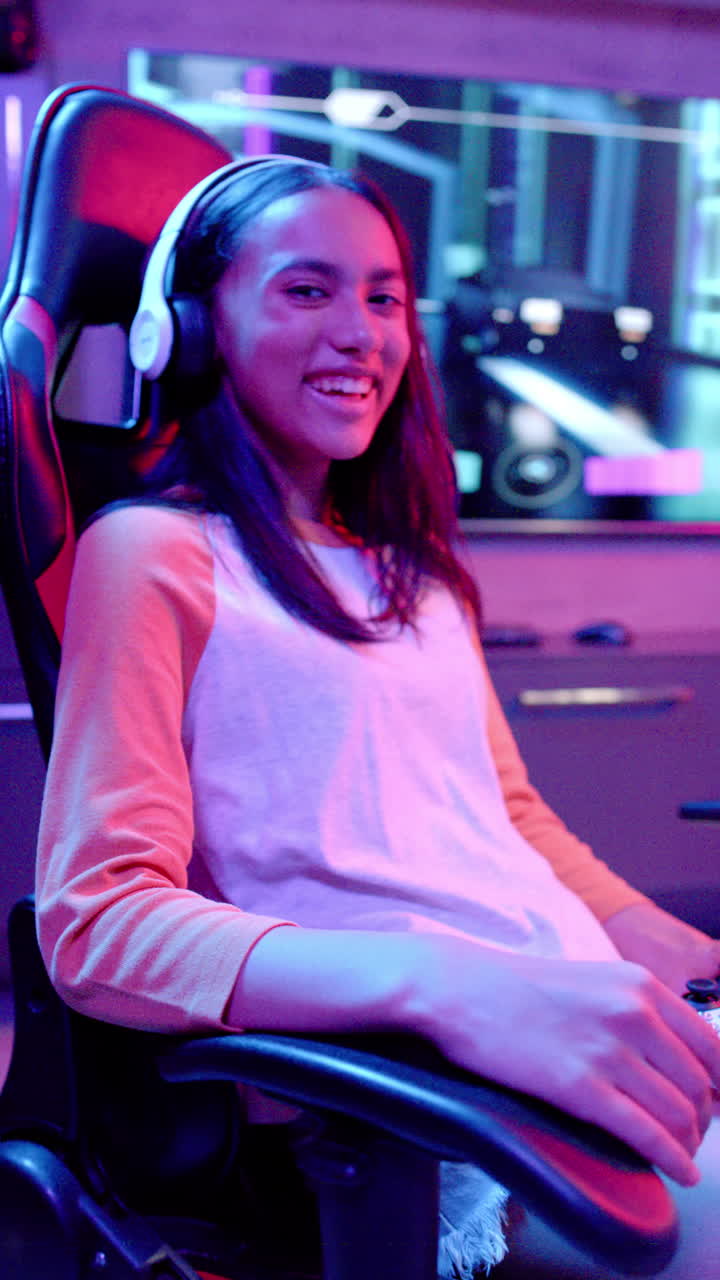 Vertical video: Teenage girl smiling while gaming with headphones in neon-lit room
