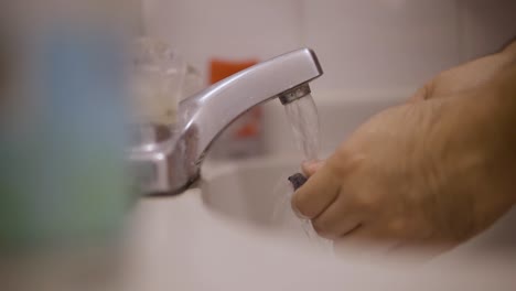 Close-up-static-shot-of-a-white-male-from-South-America-cleaning-his-toothbrush-before-putting-toothpaste-on-it-to-was-his-teeth