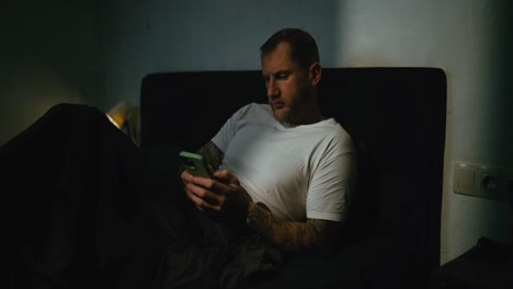 hombre usando un teléfono inteligente en la cama por la noche