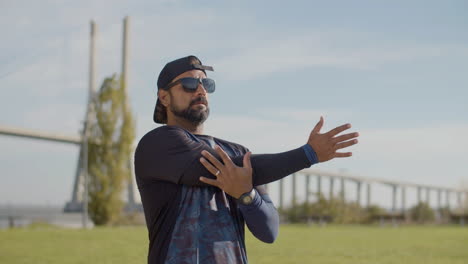 Guapo-Deportista-Con-Gafas-De-Sol-Calentando-Y-Estirando-El-Brazo-Al-Aire-Libre