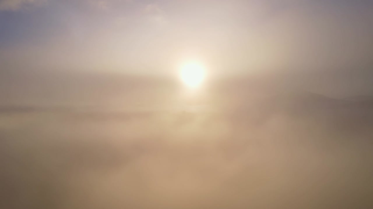 Drone view is raising above from the thick fog above the beautiful waves of fog at sunrise or sunset sky.Sun is rising above the endless clouds until the horizon. Amazing nature landscape background