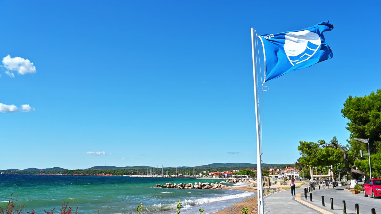 A blue flag with a sign on it near the embankment street, greenery, Aegean sea cost in Nikiti, Greece