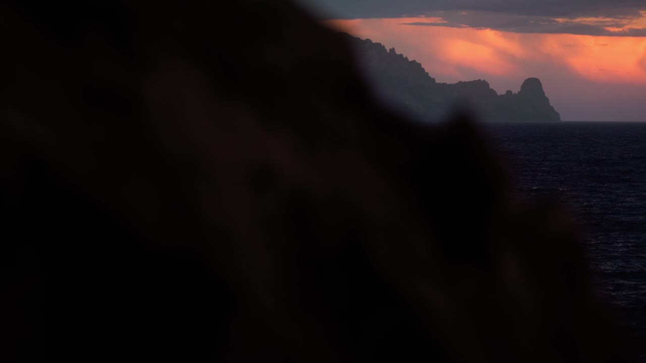 Cinematic reveal of Es Vedra at sunset in Ibiza as camera moves from behind rock to show island silhouette over Mediterranean sea