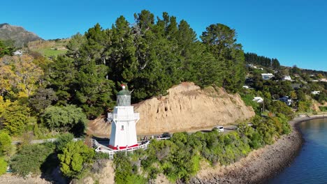 aerial footage captures akaroa lighthouse surrounded by lush greenery and calm waters under clear blue skies