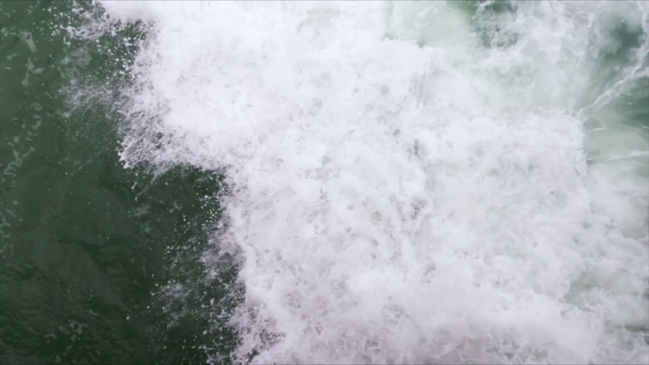 Close-up of a blue foamy wave crashing on rocks in slow motion