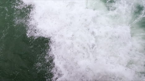 Close-up-of-a-blue-foamy-wave-crashing-on-rocks-in-slow-motion