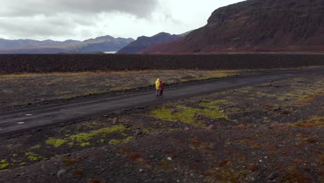 Aerial-4k-view-of-a-couple-hiking-while-holding-hands-on-a-gravel-road-with-a-beautiful-mountain-landscape-in-Iceland,-Europe,-orbit-shot