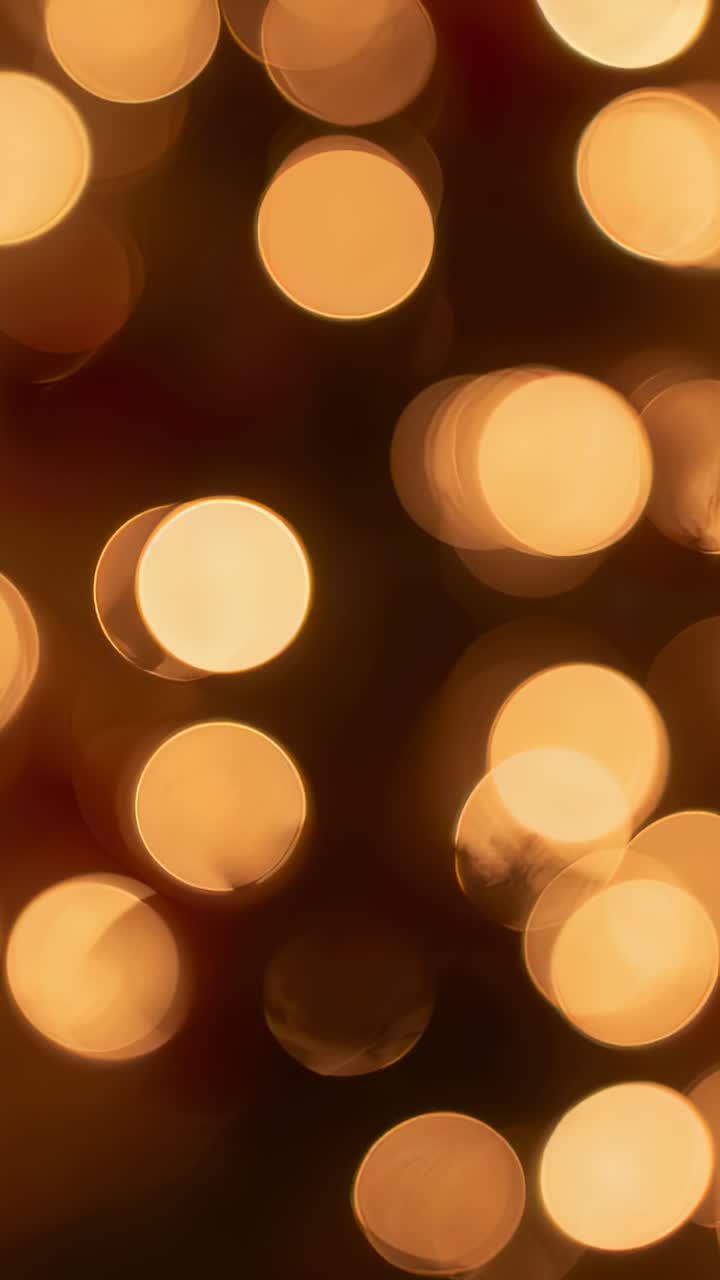 Vertical video: Shifting cam focus revealing soft gold bokeh and faint red green hints in dim room