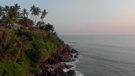 Aerial-view-of-Varkala-Beach,-Kerala,-India-showing-dense-greenery-on-the-magnificent-cliffs-along-the-seashore-with-low-tides-hitting-them