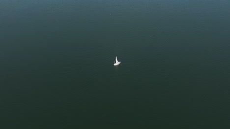 Lone-white-sailboat-with-erected-sail-in-dark-moody-green-ocean