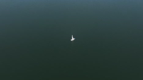 lone white sailboat with erected sail in dark moody green ocean