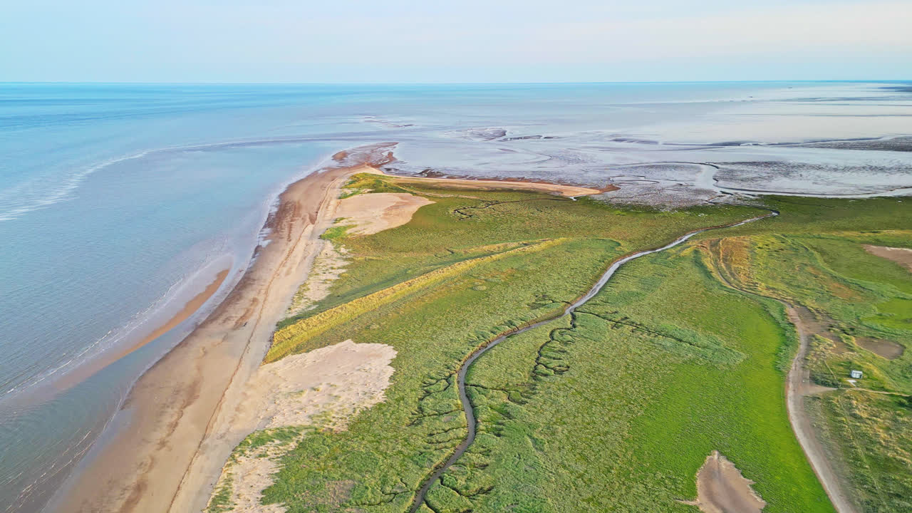 황금 시간의 해안 풍경의 이 ⁇ 한 매력을 드론으로 찍은 숨 막히는 영상으로 발견하십시오. 강 입구, 모래 언덕, 바다, 습지