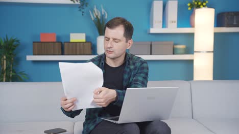 man using laptop looking at paperwork. credit extra debt papers, title deeds, property papers.