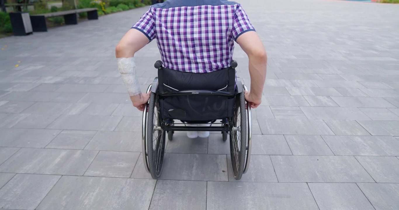 Uomo con il braccio infortunato che si muove in sedia a rotelle nel parco