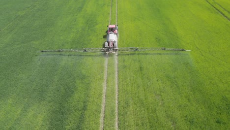 aerial following shot of the agricultural sprayer spraying insecticide to the green field on spring