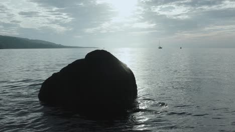 shot of rock in the ocean silhouetted in front of morning sun