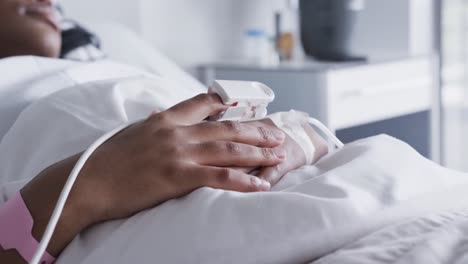 hands of african american female patient lying in bed in hospital room, slow motion