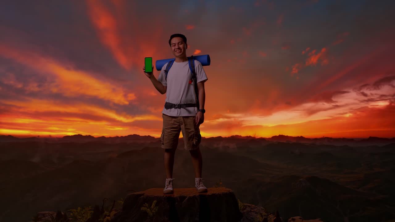 senderista feliz en la cima de la montaña al atardecer con teléfono de pantalla verde
