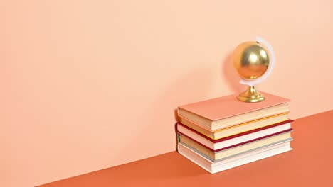 globo terrestre dorado girando en la pila de libros ordenados contra el tema naranja profundo y brillante. detener el movimiento