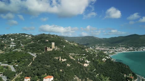 Aerial-View-Of-Italian-Coastal-Village-Of-Noli-With-Monte-Ursino-Castle-In-Background-On-Hilltop