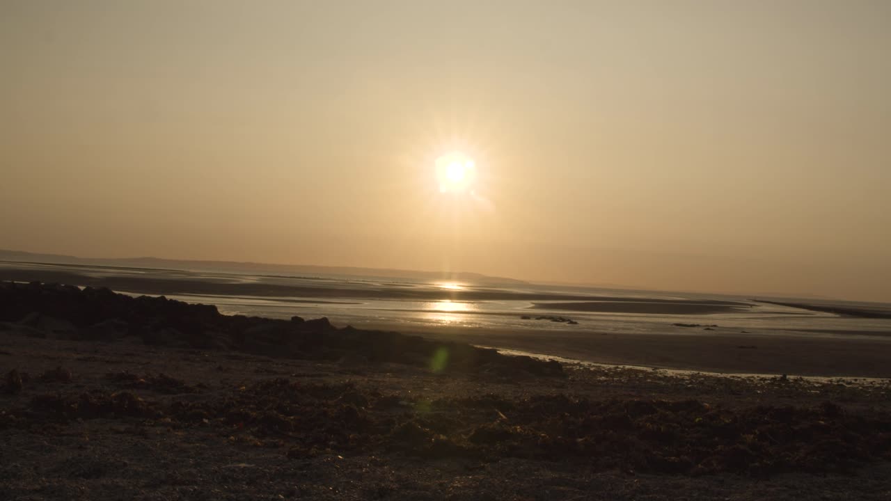 모래 위를 걷는 사람들과 함께 랜디드노 해변 위로 황금빛 일몰의 시간 경과