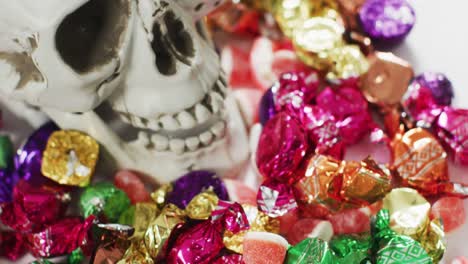 close up view of human skull and multiple candies fallen against grey background