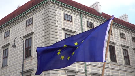 single eu flag being held up and waving against backdrop of building during protests