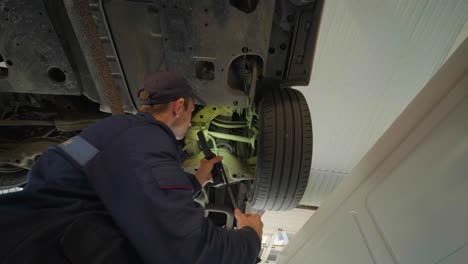 young car mechanic at repair service station inspecting car wheel and suspension detail of lifted automobile. bottom view.