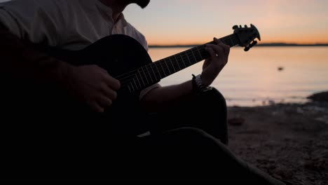 man playing guitar at sunset by the lake