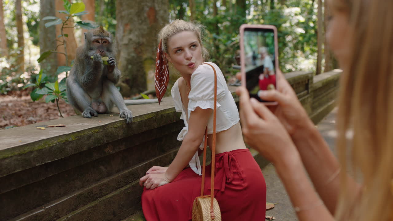 mujer turista usando un teléfono inteligente tomando una foto de su amiga posando con un mono en el zoológico de vida silvestre divirtiéndose compartiendo la aventura de viaje