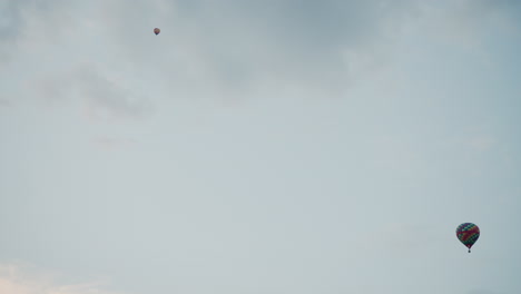 wide panoramic view of two colorful hot air balloon drifting gracefully across expansive summer sky with soft cloud formations and subtle pastel hues