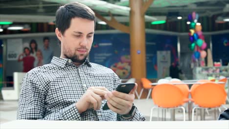 hombre usando un teléfono inteligente en una sala de comidas de un centro comercial