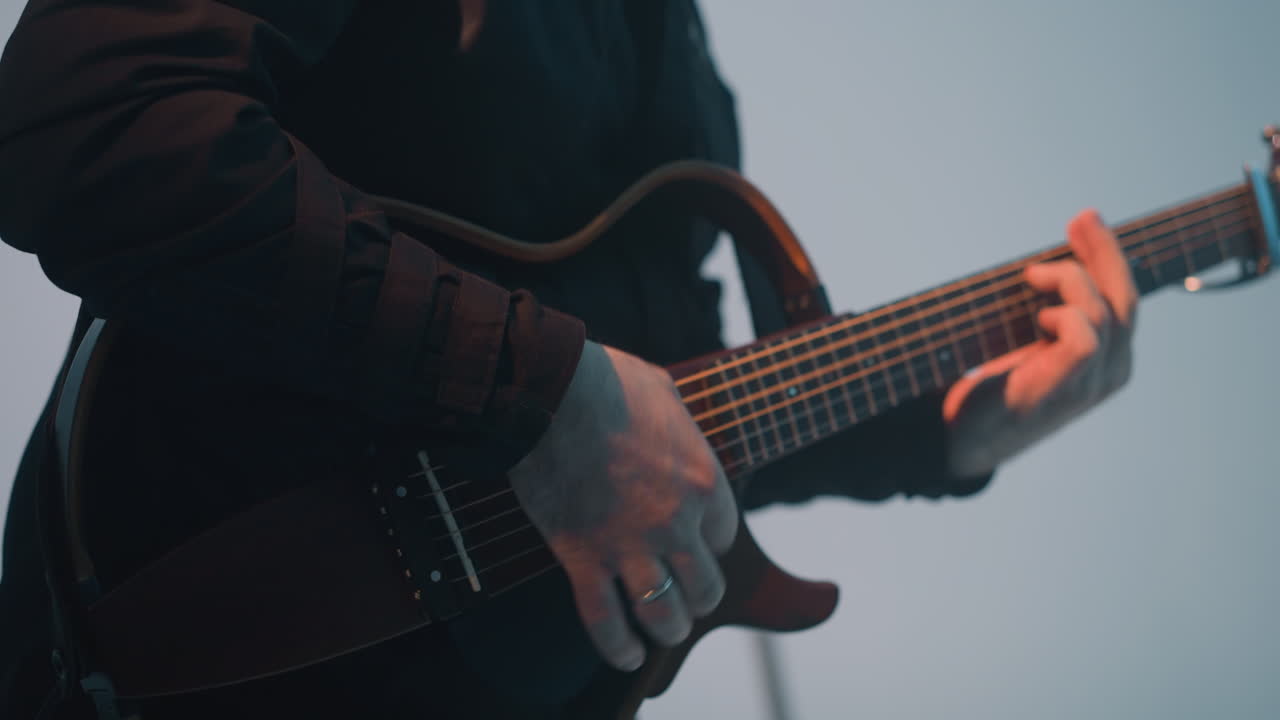 un guitarrista sin rostro está tocando una guitarra contra un fondo blanco, con otra guitarra visible en el fondo. el primer plano se centra en las manos del músico y la guitarra