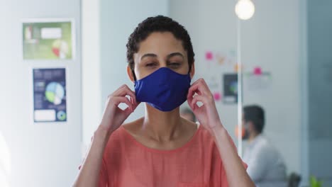 retrato de una mujer caucásica ajustando su máscara facial en una oficina moderna