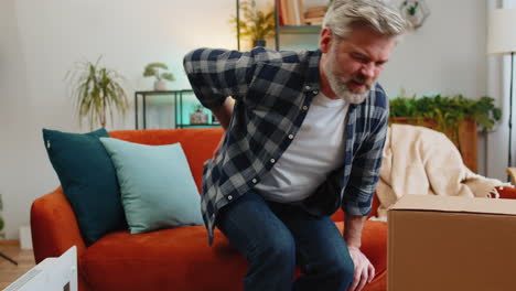 senior mature man carrying heavy box and experiences severe back pain muscle pain of overwork spasm
