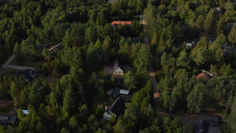 Fly-above-vacation-location.-Houses-of-cottages-between-trees-lit-by-late-afternoon-sun.-Wooded-landscape.-Denmark