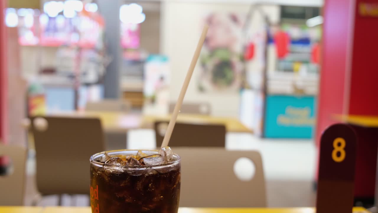 Glass with cola and ice then a white straw, queue card number, and a shop in a super supermarket and Beverage