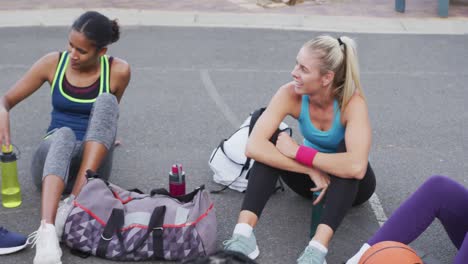 Diverso-Equipo-De-Baloncesto-Femenino-Sentado-En-El-Suelo-Y-Hablando