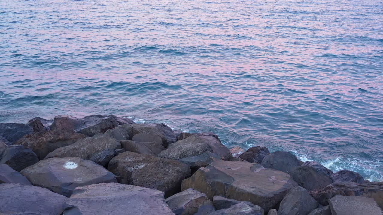 바위 가 있는 해안선 근처 의 바다 물 에 반사 되는 해 가 지는 빛