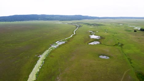 Weitläufige-Grüne-Ebene-Landschaft-Mit-Bach-,-Fluss--Und-Seewasserstraßen-Und-Bergen-Im-Hintergrund,-Luftdrohnenflug-über-Feuchtgebiete