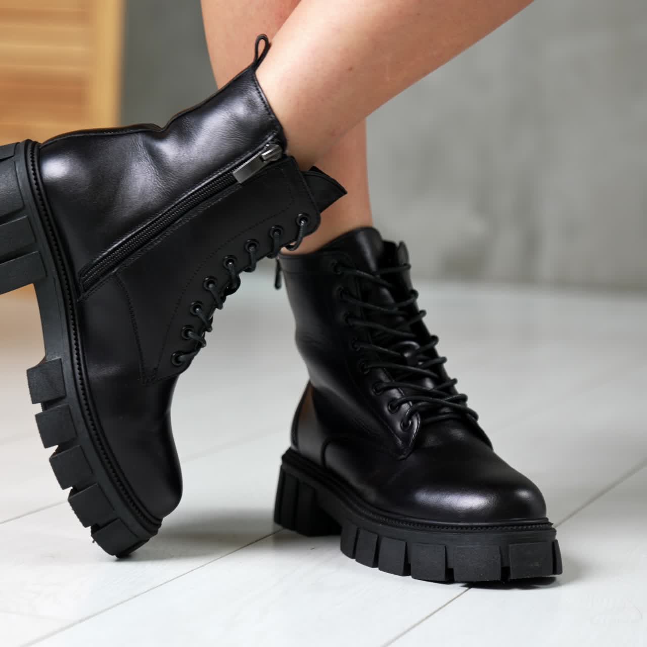 Bare-legged model demonstrating the stylish boots on tractor soles. Black leather footwear with laces close up at white backdrop