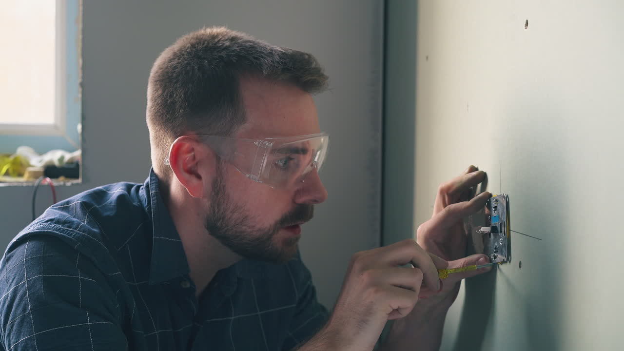 hombre enojado con gafas repara el enchufe en la pared en una habitación vacía