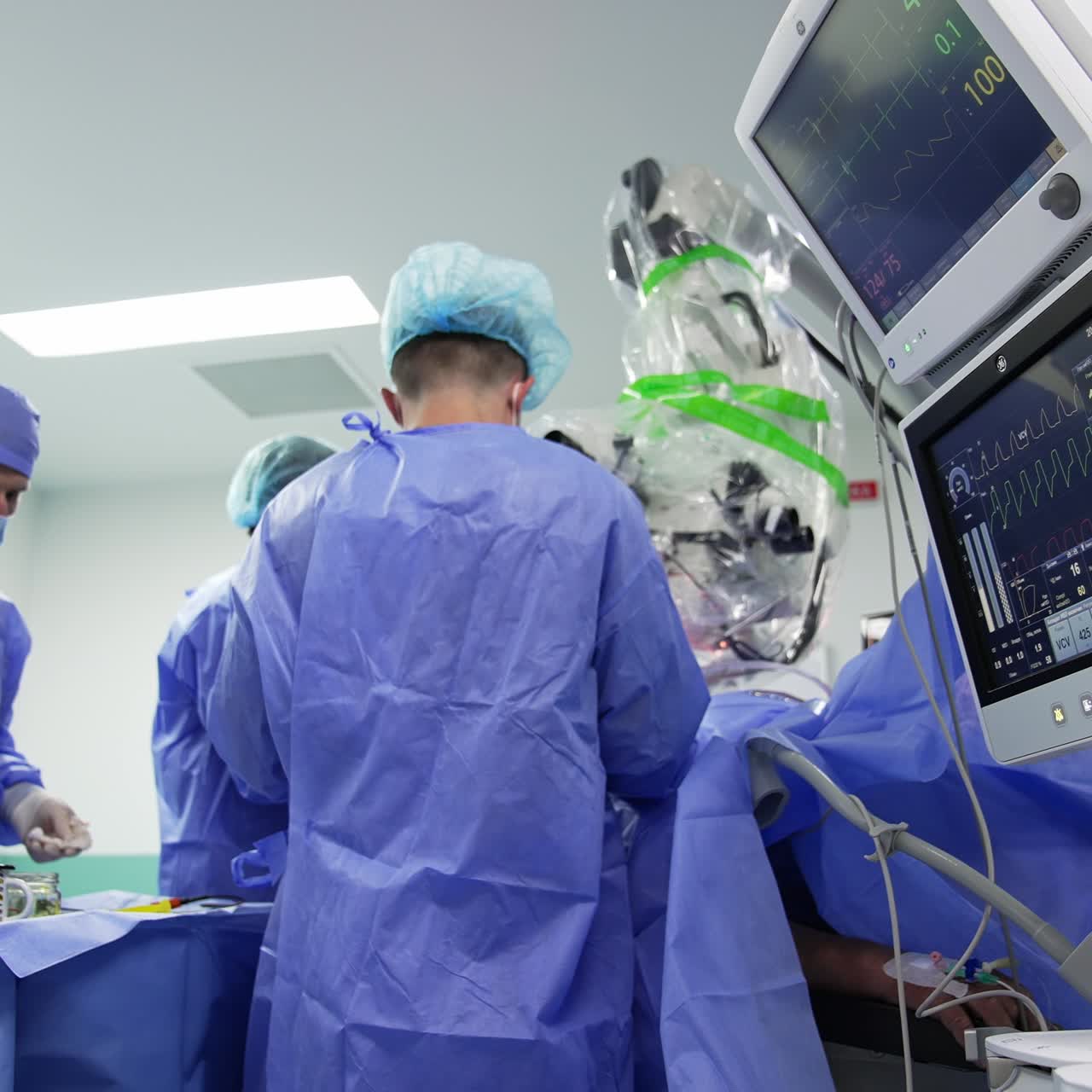 Team of doctors wearing blue uniform conducting operation. Modern equipment with screens working at foreground